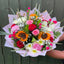 Hand holding a mixed bouquet of sunflowers, red and pink roses, carnations, white chrysanthemums and gypsophila with grass blades in blush marble wrap -- Blossom Surprise Northampton