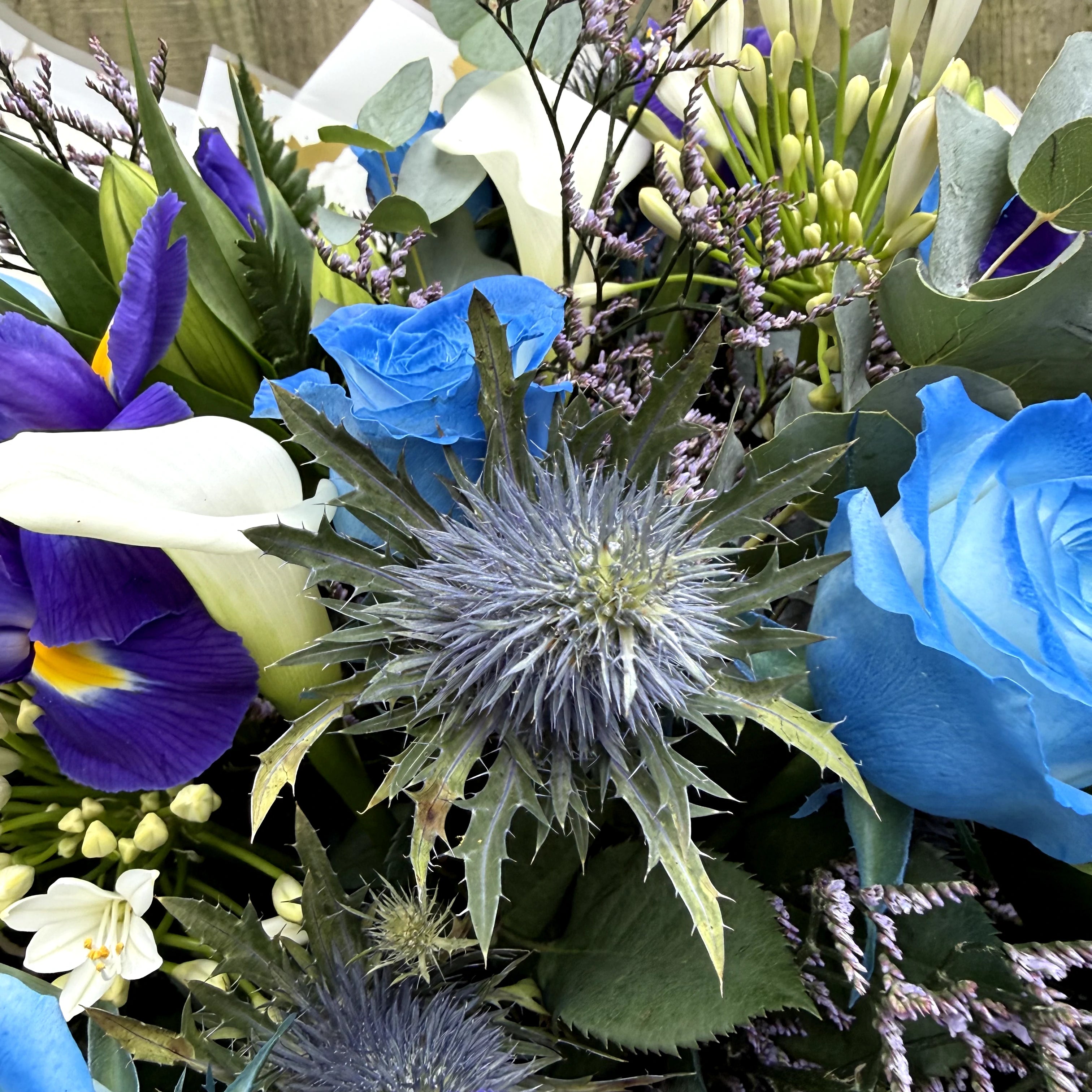 Bouquet of flowers with blue roses, purple iris, and greenery.