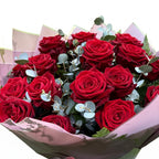 Bouquet of red roses with greenery in pink paper wrapping