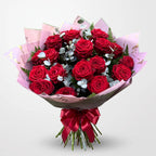 A bouquet of 20 red roses wrapped in pink patterned paper with a red satin ribbon, set against a light gray background. Blossom Surprise