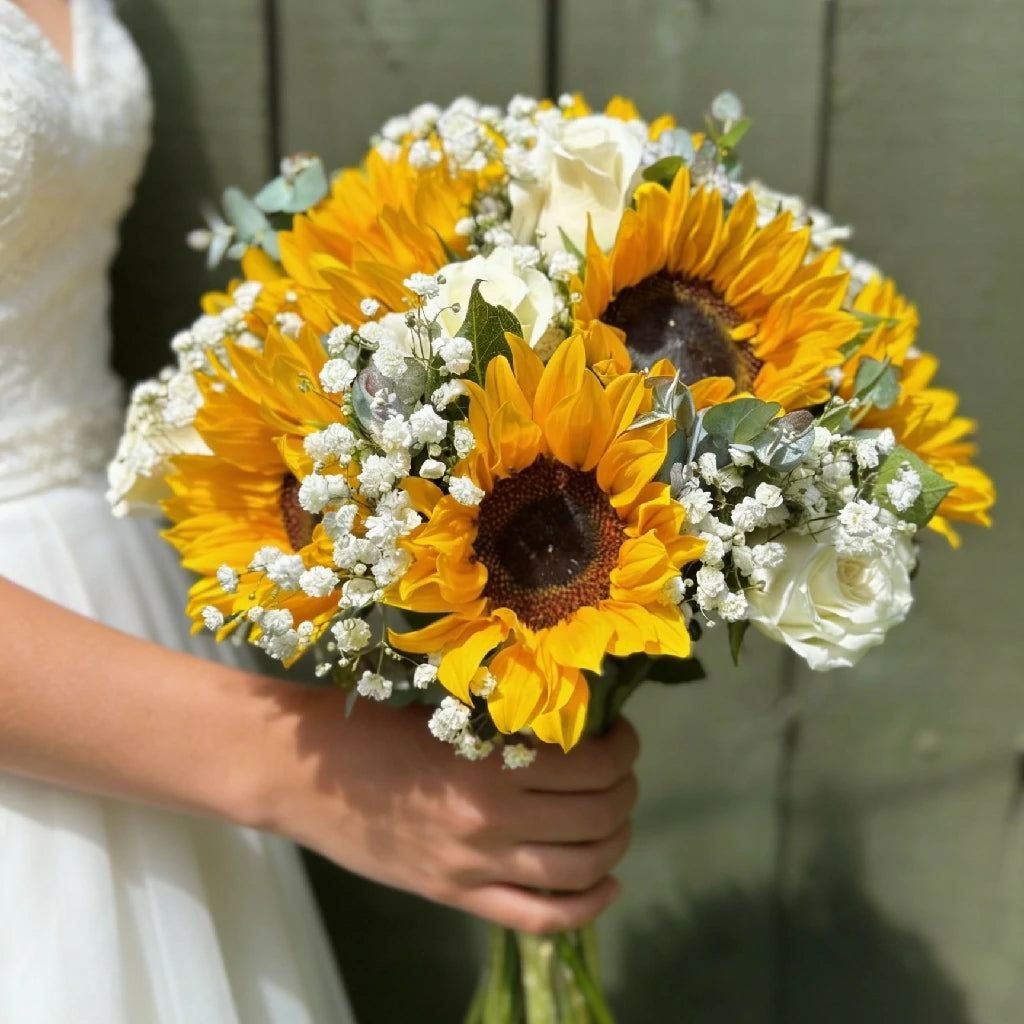 Bouquet of sunflowers and white roses held by a bride in a white dress.