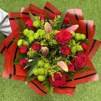 Overhead view of red rose and lime-green pompon chrysanthemum bouquet with opening pink lily buds, yellow solidago and fern in red and black luxury wrap - Blossom Surprise