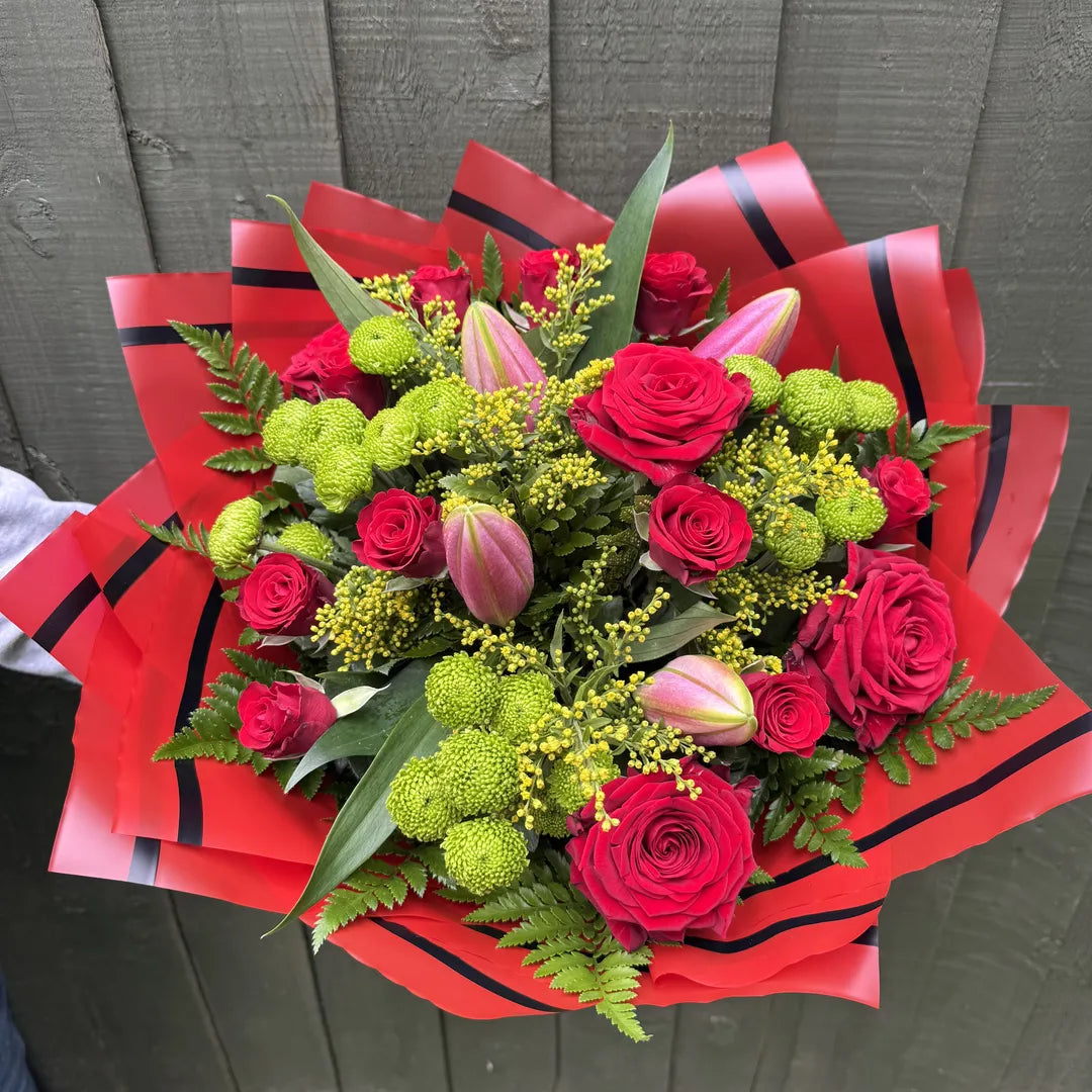 Another overhead view of red rose and lime-green pompon chrysanthemum bouquet with opening pink lily buds, yellow solidago and fern in red and black luxury wrap - Blossom Surprise