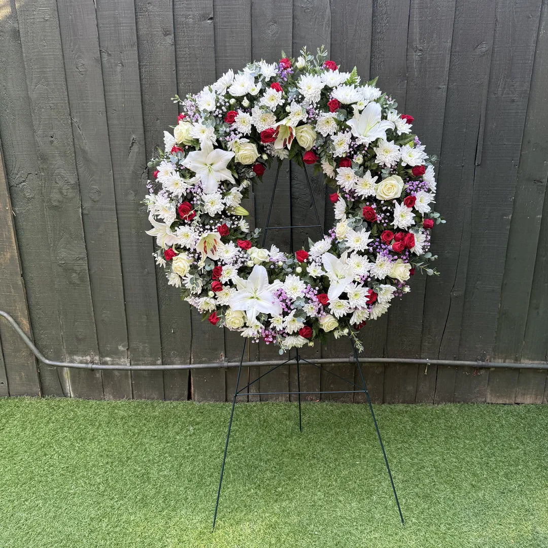 25-inch open ring funeral wreath with white oriental lilies, red roses, white chrysanthemums and purple statice on a black easel stand -- Blossom Surprise Northampton