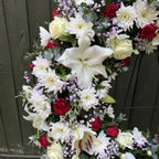 Close-up detail of funeral wreath showing white oriental lily, cream roses, red roses and purple statice with eucalyptus -- Blossom Surprise Northampton