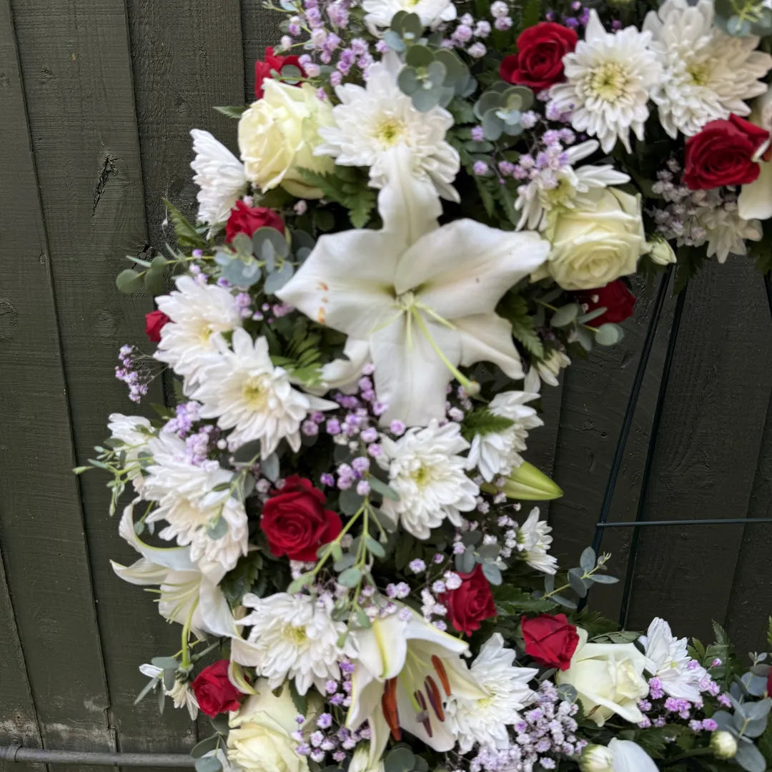 Close-up detail of funeral wreath showing white oriental lily, cream roses, red roses and purple statice with eucalyptus -- Blossom Surprise Northampton