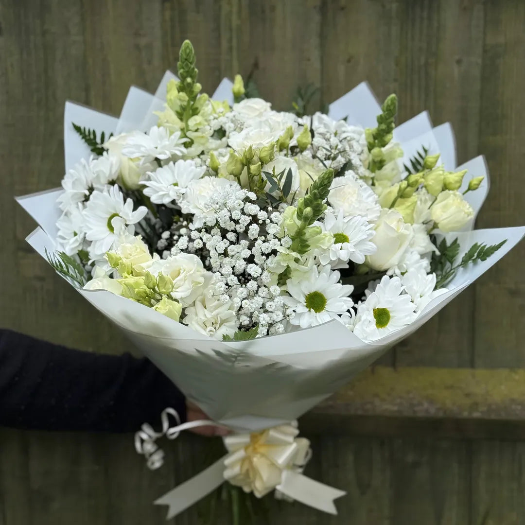 Hand holding a large all-white bouquet of roses, lisianthus, chrysanthemums, snapdragons, carnations and gypsophila in white wrap -- Blossom Surprise Northampton