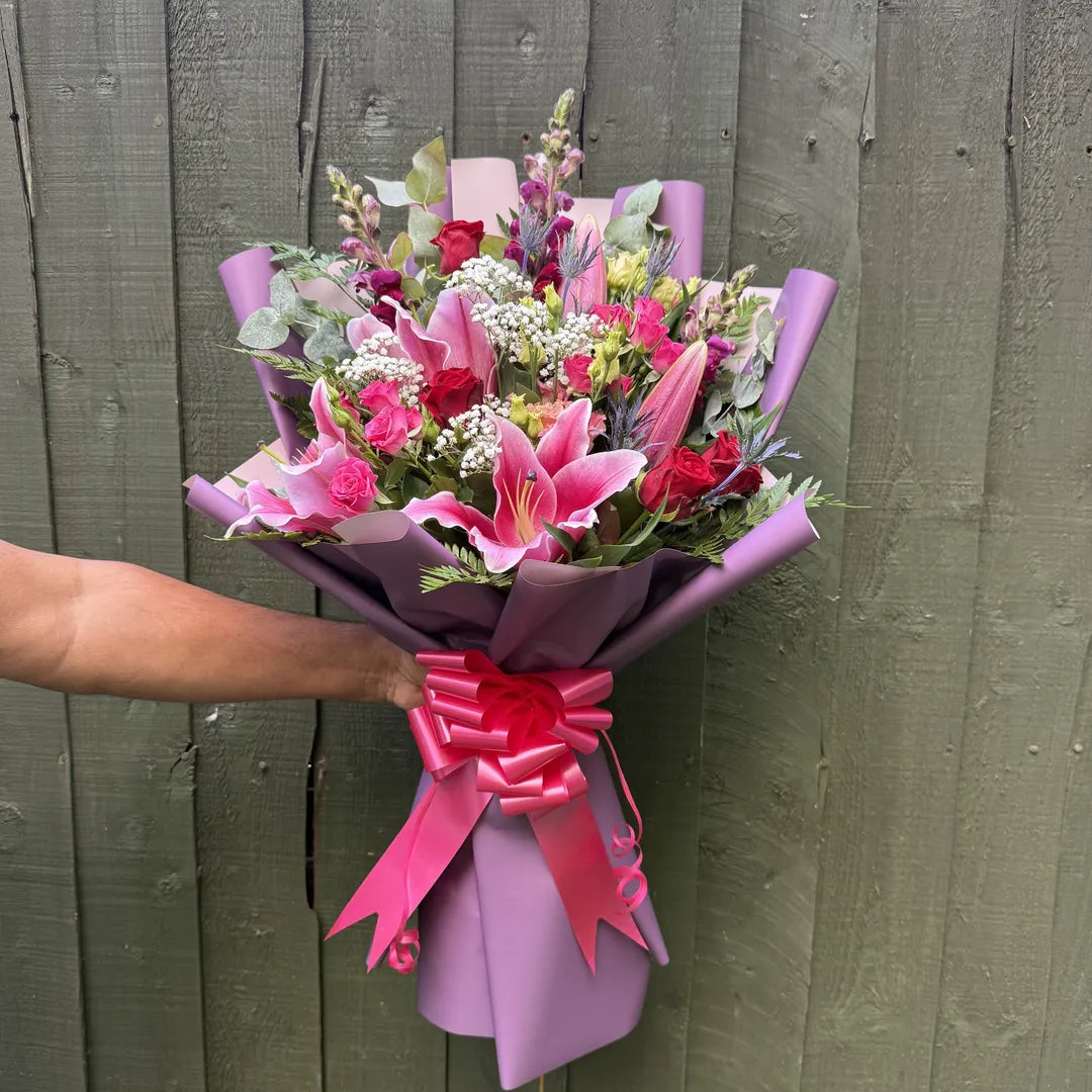 Hand holding a stargazer lily, red rose and thistle bouquet with purple snapdragons and gypsophila in purple marble wrap -- Blossom Surprise Northampton