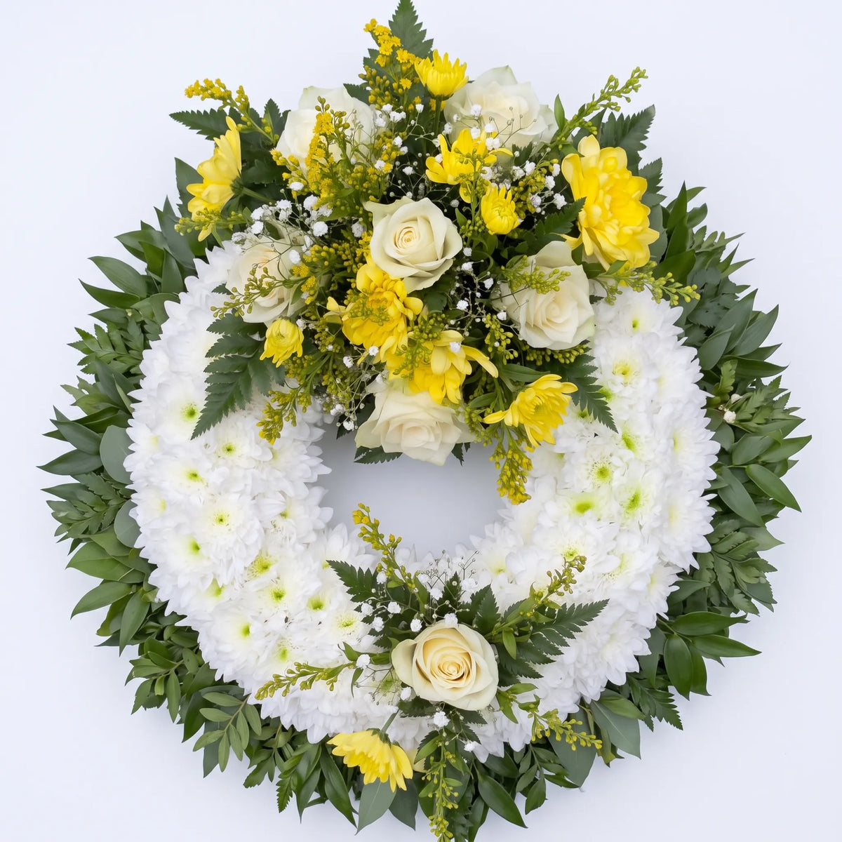 A circular floral wreath with a white chrysanthemum base, accented by yellow and white roses, yellow carnations, and green foliage on a plain white background.